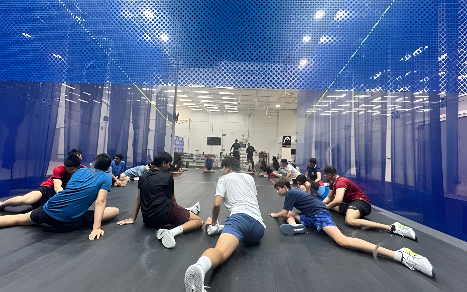 People stretching on a squash court floor.